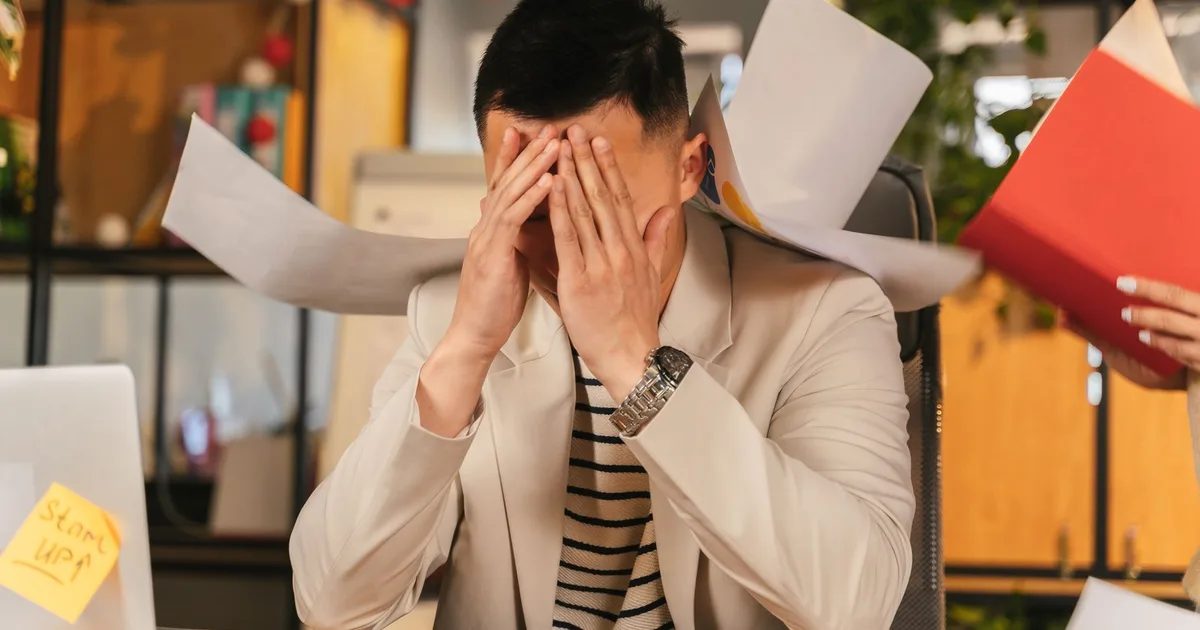 Overwhelmed business owner covering her face as papers fly around her desk