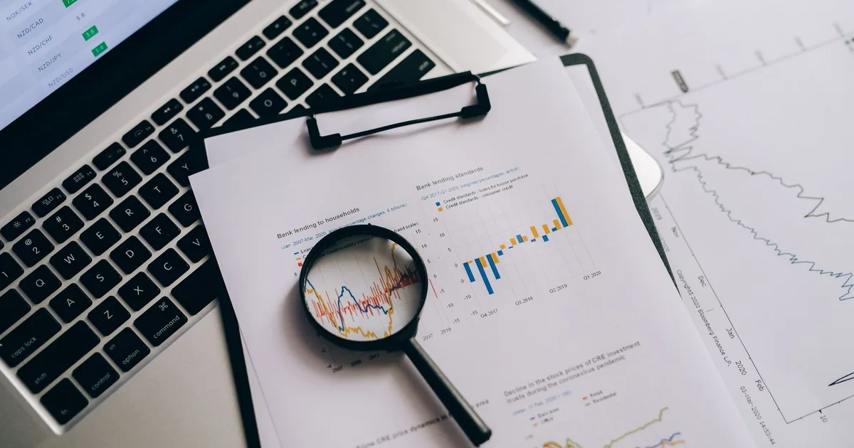 Magnifying glass over printed profit charts next to a laptop