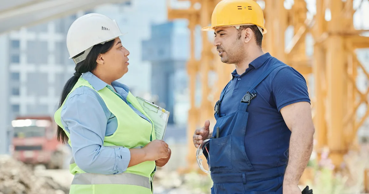 Two workers in hard hats and safety vests having a conversation at a construction job site before crews mobilize