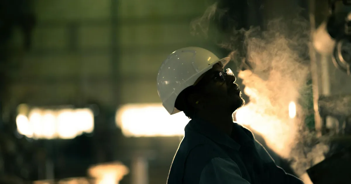 Industrial worker in hard hat surrounded by steam on a job site, representing an owner still physically on the tools in a field-based restoration business