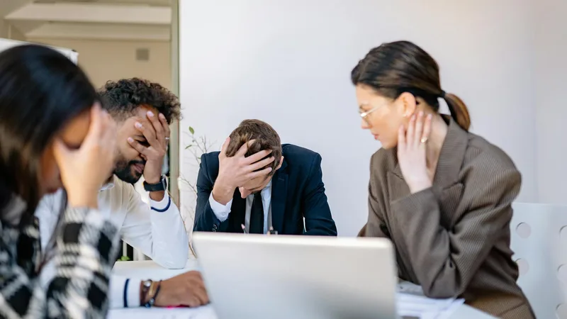 Stressed team members with heads in hands around a table, representing the overwhelm restoration owners feel when the business outgrows their systems