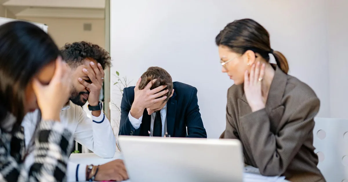 Stressed team members with heads in hands around a table, representing the overwhelm restoration owners feel when the business outgrows their systems